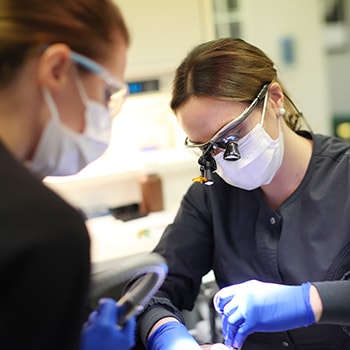 Two dentists wearing masks and gloves performing a procedure on a patient outside the frame