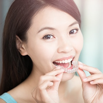 A smiling woman inserting a night guard into her mouth