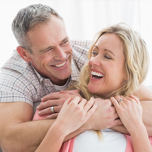 A happy couple hugging one another and showing off natural, white smiles