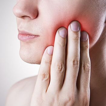 A man rubbing his cheek due to a painful dental emergency