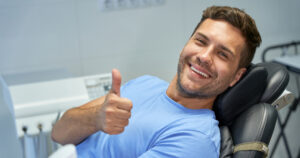 Man sitting in dentist’s chair giving the camera a thumbs up over a positive dental experience